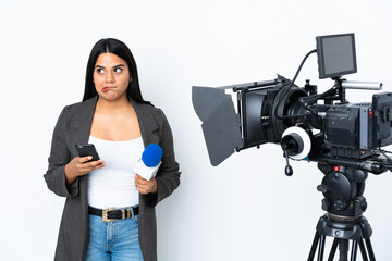 Wall Mural - Reporter Colombian woman holding a microphone and reporting news on white background holding coffee to take away and a mobile while thinking something