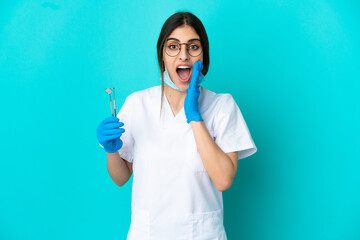 Canvas Print - Young caucasian dentist woman holding tools isolated on blue background with surprise and shocked facial expression