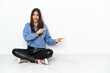 © luismolinero - Young woman sitting on the floor isolated on white background surprised and pointing side
