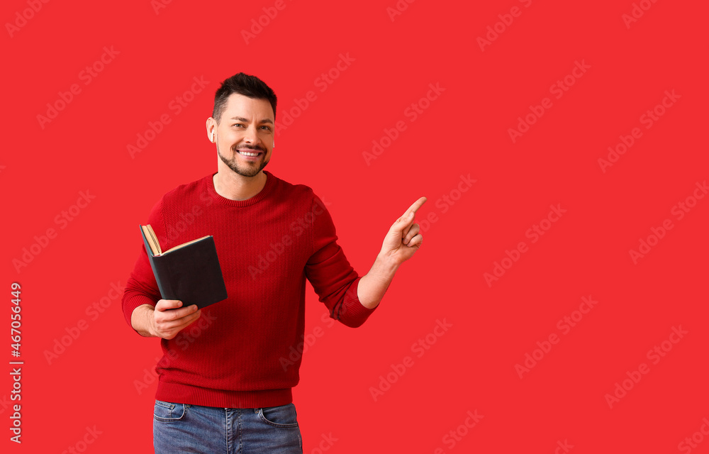 Man with earphones and book pointing at something on color background