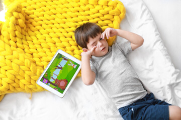 Sticker - Tired little boy watching cartoons on tablet computer in bedroom