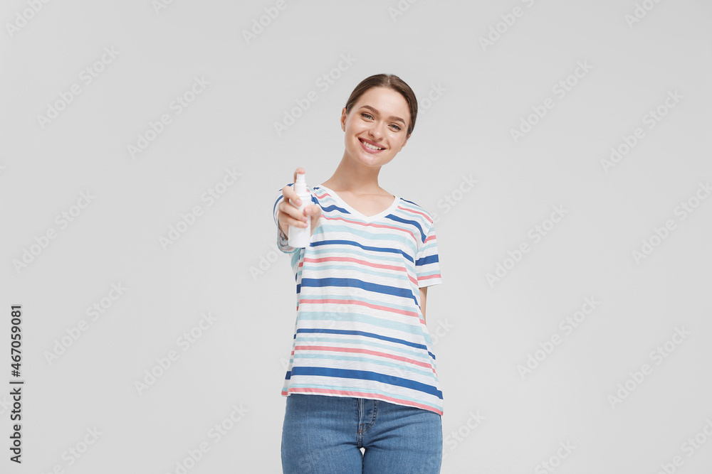 Young woman with mosquito repellent on light background