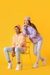 Wall Mural - Stylish young couple in hoodies on yellow background