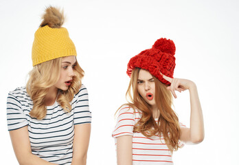 Wall Mural - two female friends in colorful hats are standing next to each other posing light background