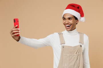 Wall Mural - Young happy african man 20s wear Santa Claus red Christmas hat doing selfie shot on mobile cell phone isolated on plain pastel beige background studio portrait Happy New Year 2022 celebration concept