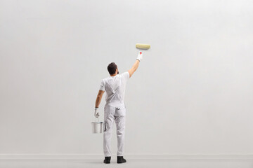 Poster - Rear view shot of a painter holding a bucket and painting a wall