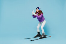 Full Length Skier Woman Wearing Warm Purple Padded Windbreaker Jacket Ski Goggles Mask Spend Extreme Weekend In Mountains Use Hold Mobile Cell Phone Chatting Isolated On Plain Blue Background Studio