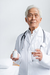 Wall Mural - Senior asian doctor holding glass of water and jar with pills in hospital ward