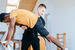 © Iryna - Fitness instructor corrects and controls the Pilates exercise that his african american male student is doing on Reformer bed in health center, gym with modern interior.