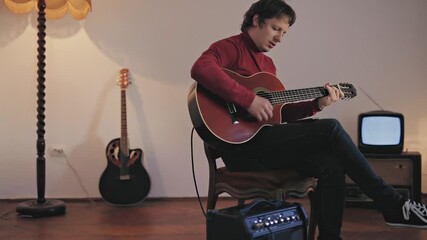 Wall Mural - Male musician playing acoustic guitar on the amplifier in retro vintage room.	
