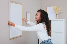 Happy African American Woman Hanging Empty Frame On Pale Rose Wall In Room. Mockup For Design