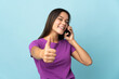 © luismolinero - Teenager girl isolated on pink background keeping a conversation with the mobile while doing thumbs up