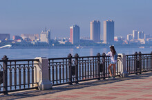 A Young Girl With A Backpack Admires The View Of The City Of Heihe, China From The Embankment Of The City Of Blagoveshchensk, Russia. Focus On The Foreground.