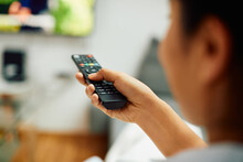 Close-up Of Woman Watching TV And Changing Channels With Remote Controller At Home.