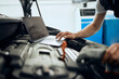 © Drazen - Close-up of auto mechanic uses laptop while examining car engine at service workshop.