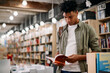 © Drazen - Young African American student reads book while standing at bookstore.