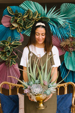 Smiling Hispanic Female Florist Standing On Veranda With Creative Floral Arrangement