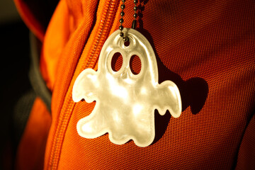 Elegant white reflective safety signal in a ghost pattern form on an orange backpack for pedestrian visibility