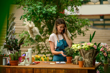 Wall Mural - Florist talking with client on the smartphone and taking an order in a flower shop