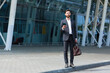 © Liubomir - stylish bearded business man with travel bag and mobile phone in hands walks on city street modern urban background. Businessman in a suit goes and uses a smartphone. tourist trip. caucasian manager