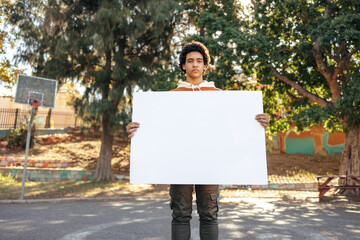 Teenage boy holding a blank placard in a park