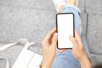 Young woman sitting on stairs and using modern mobile phone outdoors, closeup