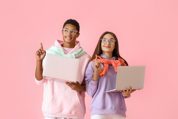 Wall Mural - Stylish young couple in hoodies with laptops pointing at something on pink background