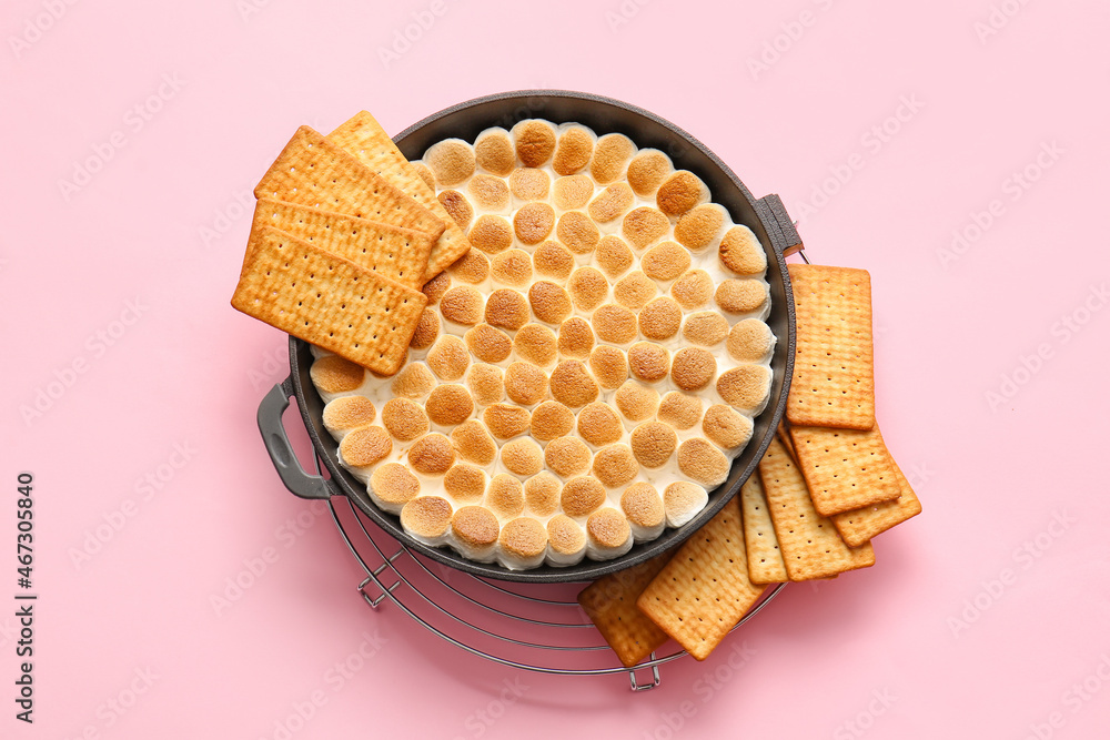 Frying pan with tasty S'mores dip and crackers on pink background