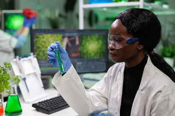 African american biologist researcher holding medical test tube with green solution working at biochemistry experiment in biochemistry hospital laboratory. Chemist analyzing geneticaly modified liquid