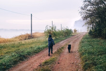 Boy And Dog In The Forest. A Cocker Spaniel Is Running Alongside The Child Along A Country Road. Walk With A Black Pet Among The Autumn Trees.