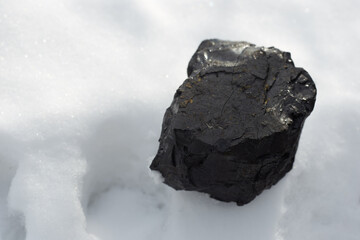 The black coal stone lying on the white snow symbolizes energy, warmth and wealth