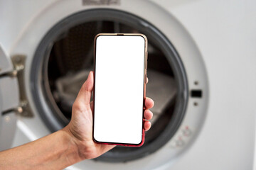 Wall Mural - a person hand holding a smartphone with blank screen near the washing machine. woman controlling was