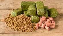 Pelleted Horse Feed On Left, Green Alfalfa-timothy Cubes In The Middle, And Pink Peppermint Treats On The Right; On Rustic Wooden Table