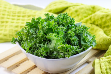 Fresh green curly cabbage or kale salad leaves cut in the bowl on light background on the table in the kitchen.