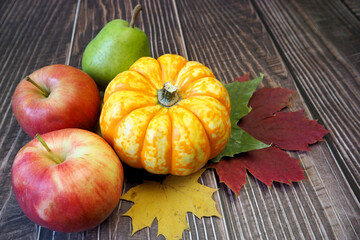 Wall Mural - a small yellow pumpkin, two red apples and a green pear lie on yellow and red maple leaves on a wooden background. side view