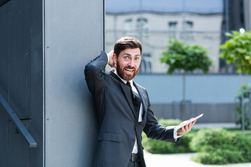 Mad unhappy businessman feeling annoyed using digital tablet smart phone. Angry business man having problem with mobile spam message. Male user frustrated by low battery or bad signal office outside