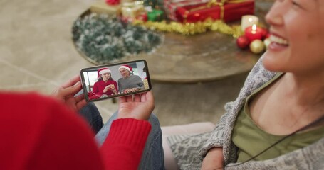 Wall Mural - Smiling asian couple using smartphone for christmas video call with family on screen