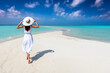 © moofushi - A woman in a white summer dress walks on a tropical paradise beach with turquoise sea and sunshine
