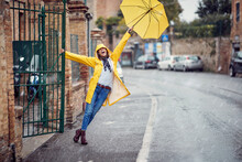A Young Girl With Yellow Raincoat And Umbrella Is Having A Good Time While Walking The City On The Rain. Walk, Rain, City