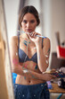 © luckybusiness - A young sexy and attractive female artist in a bra is standing in front of the easel in her studio and posing for a photo. Art, painting, studio