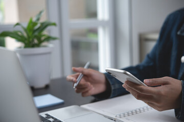 Canvas Print - Young business woman sitting at table, writing notes on notebook, using mobile phone and working on laptop computer at home office. Student learning online class, E-learning, online study