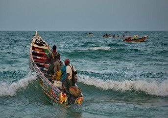 Wall Mural - Nouakchott. Mauritania. Struggling with the waves of the surf, fishermen daily sail out on special wooden boats with a motor for several days in the open Atlantic Ocean for fishing.