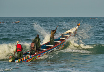 Wall Mural - Nouakchott. Mauritania. Struggling with the waves of the surf, fishermen daily sail out on special wooden boats with a motor for several days in the open Atlantic Ocean for fishing.