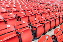 Rows Of Empty Red Bleacher Seats In A Stadium With Numbers Inside Of Baseball Looking Stickers.