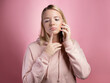 © Alexander - To think about a proposal, a young woman is talking on the phone, thoughtful or doubtful. An attractive young woman in a pink hoodie uses a smartphone, a photo on pink.