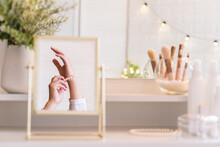 Reflection In Table Mirror Of Woman Hand  In Pearl Bracelets. Female Party Preparation. Сhristmas, Light Bulbs, Eucalyptus, Fir,  Pine Branches In A Vase  On Dressing Table With Make Up Accessories.