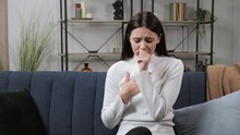 Portrait Of Ill Woman Sitting On Sofa At Home. Young Woman Coughing On The Couch. Close Up Of Sick Girl Cough Cold. Female Person Face With Flu Symptoms. Closeup Of Brunette Woman Squeezing.