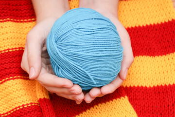 Wall Mural - blue skein of wool in hands on a yellow-red knitted tablecloth