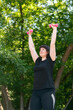 © somemeans - Girl coach performs exercises with dumbbells in the park. Outdoor fitness. Hand training with dumbbells. For beginners