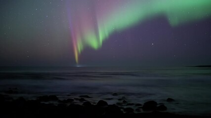 active red and green aurora borealis over ocean waves